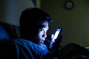 Ilustrasi seseorang scrolling ponsel di tempat tidur dengan ekspresi cemas