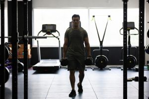 Seseorang melakukan farmer's carry sebagai simulasi latihan HYROX di gym