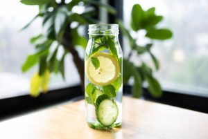 infused water lemon timun mint dalam botol kaca dengan latar belakang kayu dan daun segar