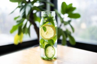 infused water lemon timun mint dalam botol kaca dengan latar belakang kayu dan daun segar