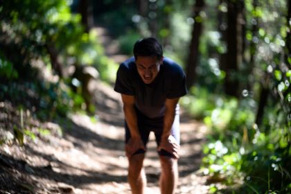 A beginner runner struggling while running uphill on a forest trail, heavy breathing, tired expression, morning sunlight, motion blur on legs, realistic style, 16:9 aspect ratio