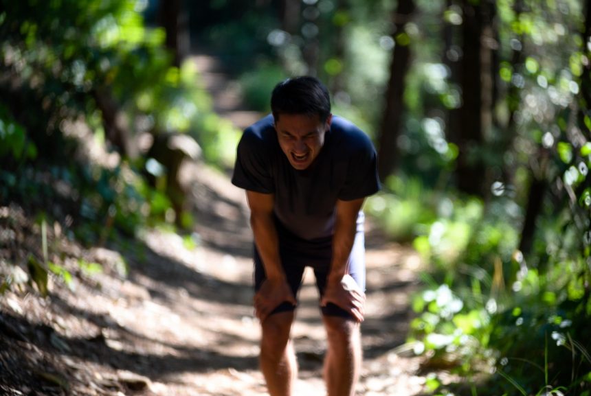 A beginner runner struggling while running uphill on a forest trail, heavy breathing, tired expression, morning sunlight, motion blur on legs, realistic style, 16:9 aspect ratio