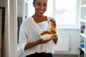 Wanita muda membawa bekal sehat ke kantor dengan wadah makan siang